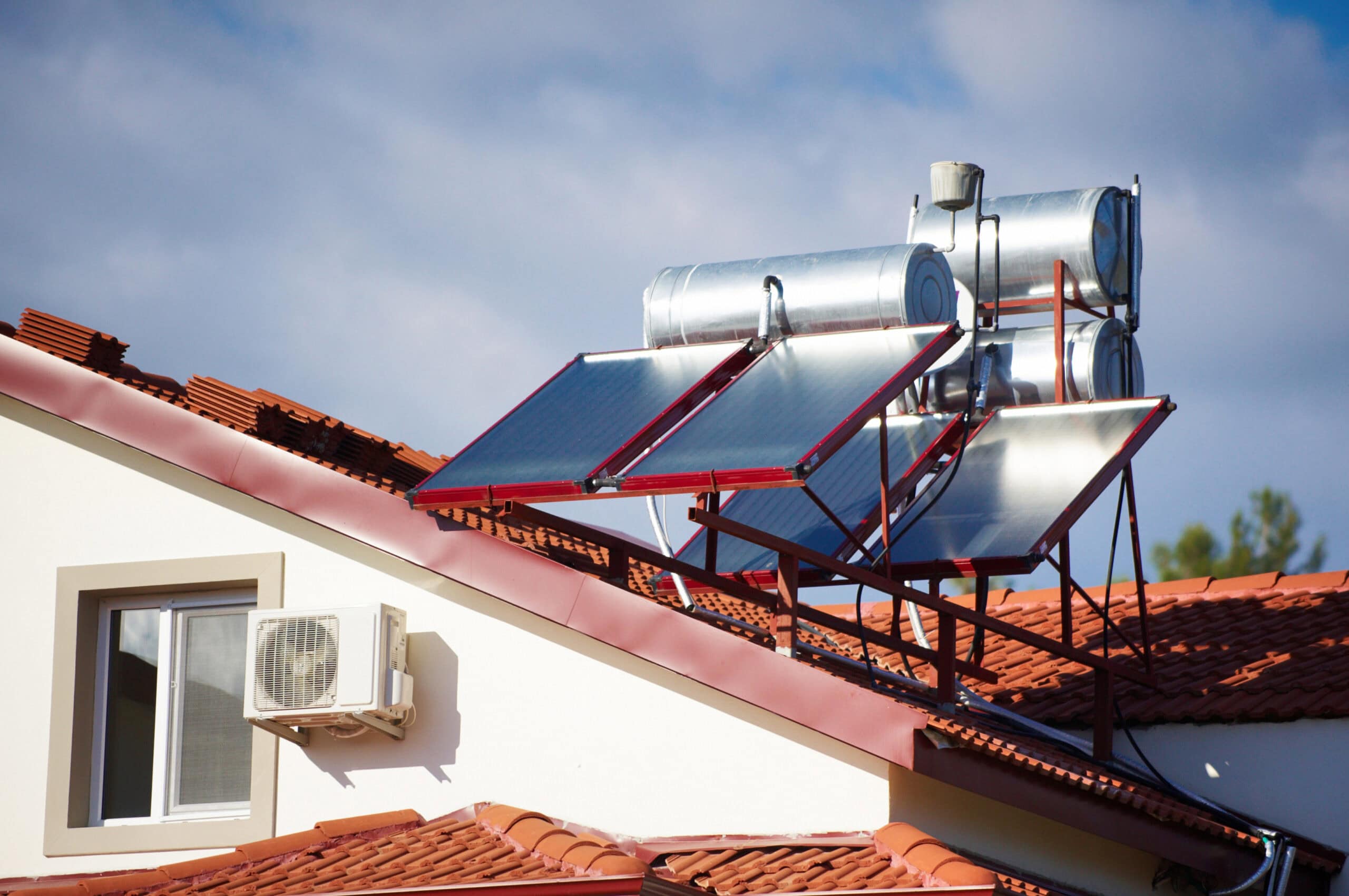 Solar hot water heaters on the roof of the house against blue sky.